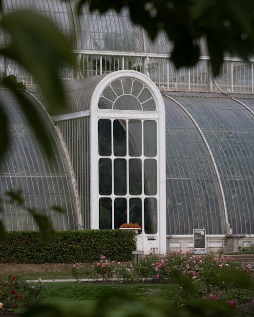 A traditional red-brick house with a steeply pitched roof and white-framed windows, situated in a landscaped garden. The front garden features a neatly trimmed hedge bordering a lush green lawn, with